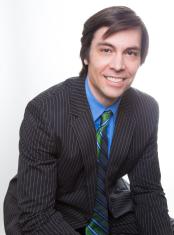 Director Chris Pettingill | a man smiling with dark hair wearing a dark suit with a light blue dress shirt